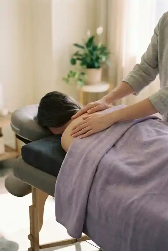 Massage therapist's hands resting on a client's shoulder on a vibroacoustic mat